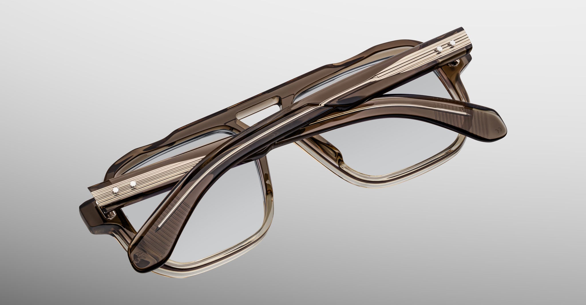 Two pairs of Jacques Marie Mage Evans handcrafted optical glasses with brown oversized acetate frames are stacked against a gradient gray background, showcasing a refined Jacques Marie Mage aesthetic.