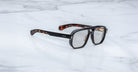 The Jacques Marie Mage Evans optical glasses, featuring an oversized brown tortoiseshell acetate frame, are elegantly displayed on a white marble surface.