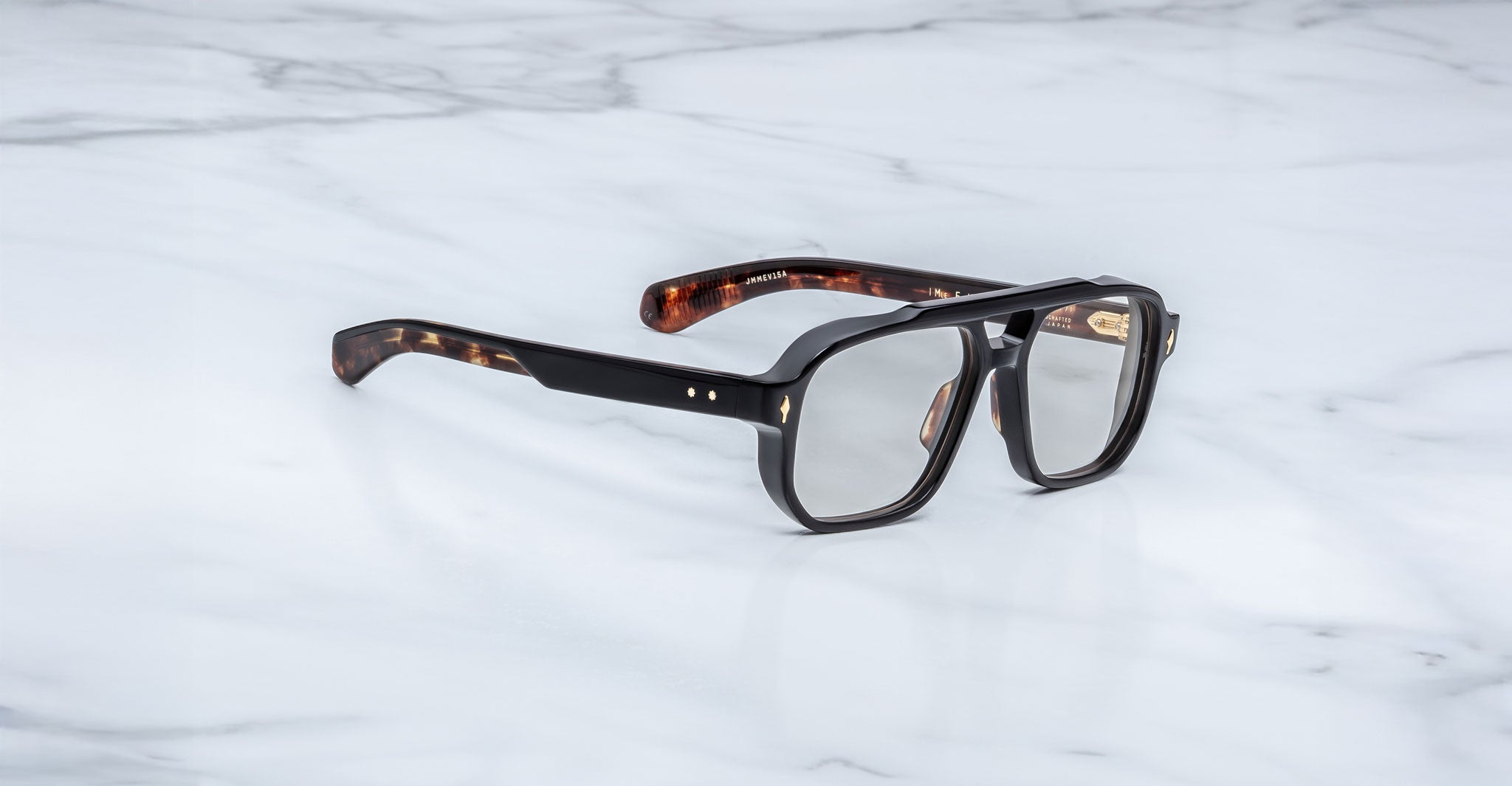 The Jacques Marie Mage Evans optical glasses, featuring an oversized brown tortoiseshell acetate frame, are elegantly displayed on a white marble surface.