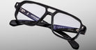 Jacques Marie Mage Evans eyeglass frames in black acetate with an oversized rectangular shape and clear lenses are displayed against a light gray background, featuring visible inner branding on the temples.