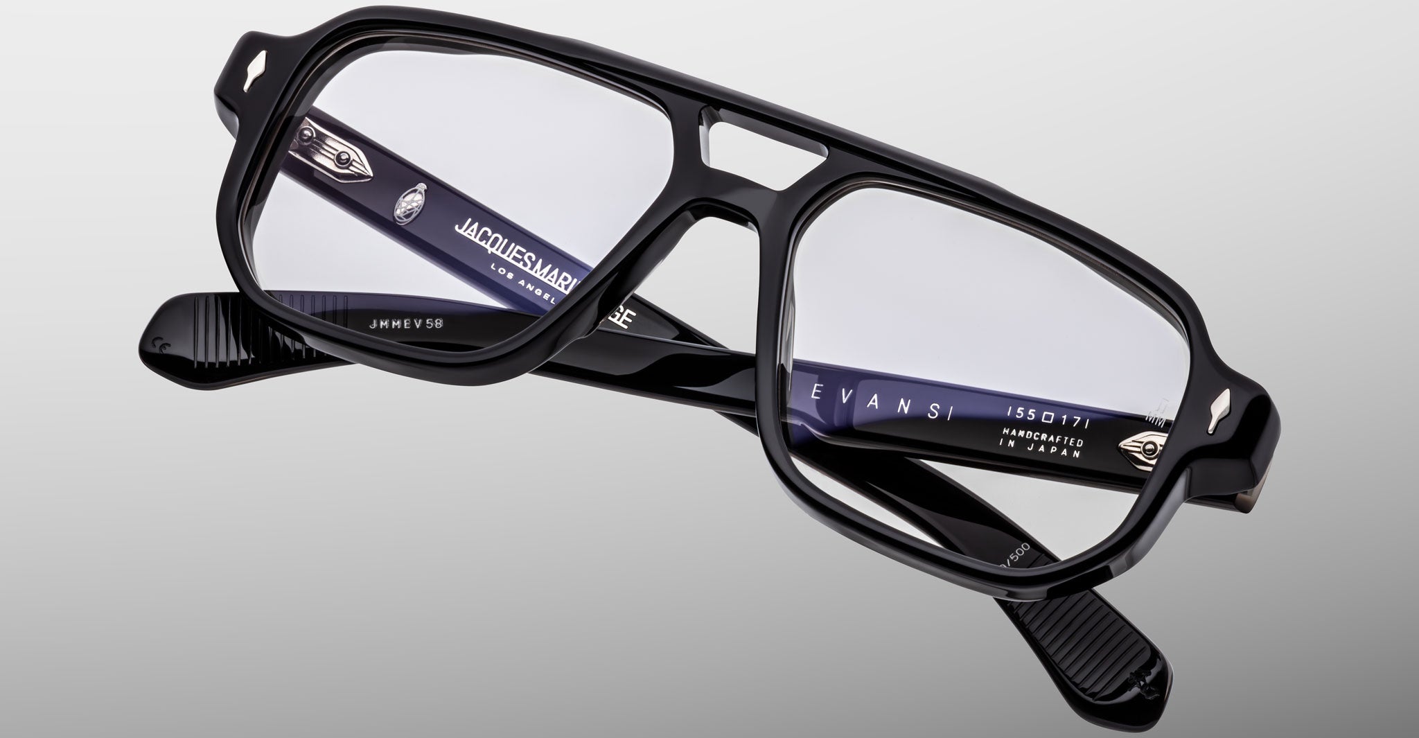 Jacques Marie Mage Evans eyeglass frames in black acetate with an oversized rectangular shape and clear lenses are displayed against a light gray background, featuring visible inner branding on the temples.