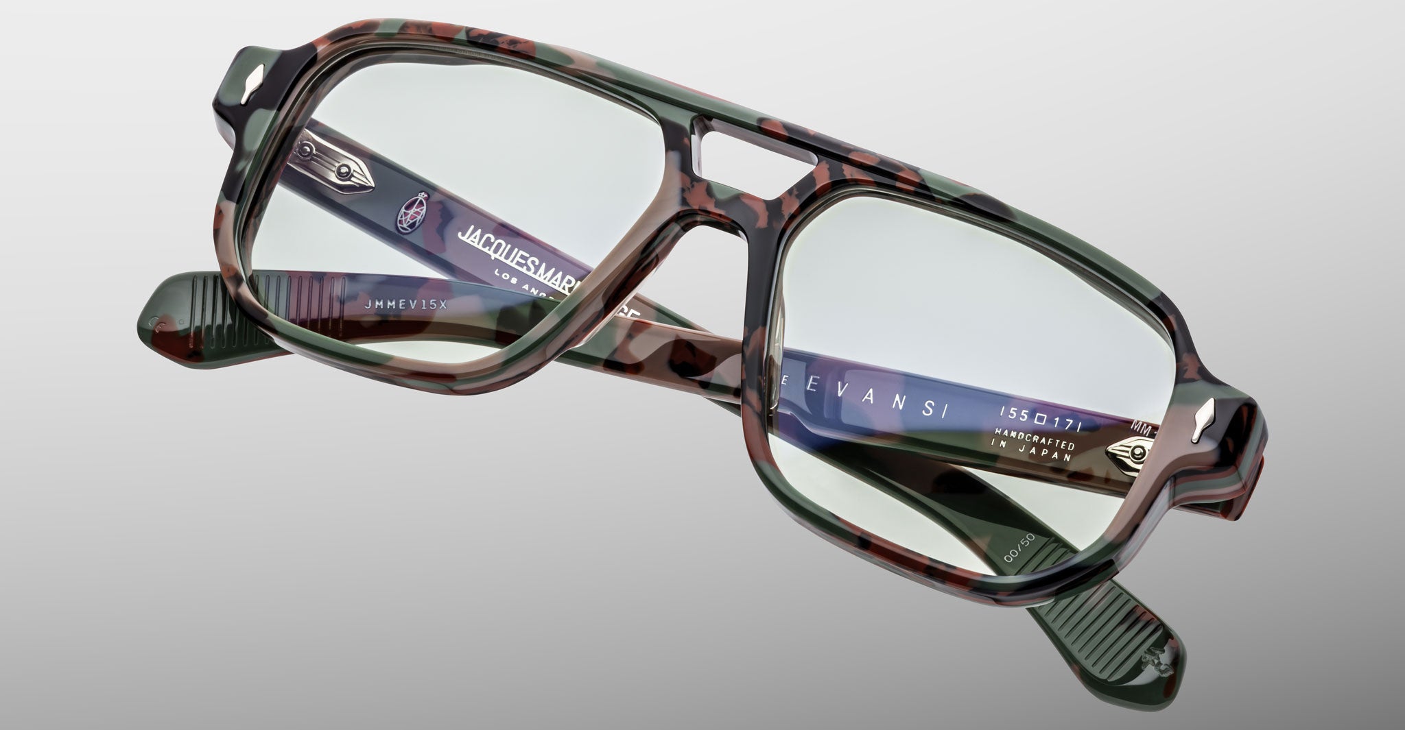 Close-up of Jacques Marie Mage Evans optical glasses by Jacques Marie Mage, featuring a rectangular camouflage design, clear lenses, metallic arm details, and an oversized acetate frame set against a light gray background.