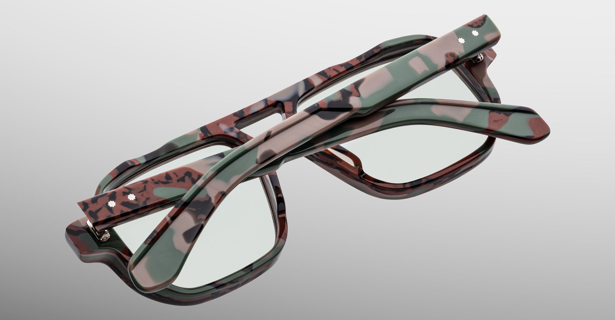 Two pairs of Jacques Marie Mage Evans optical glasses, featuring handcrafted oversized acetate frames, are stacked in a crisscross arrangement on a light grey background.