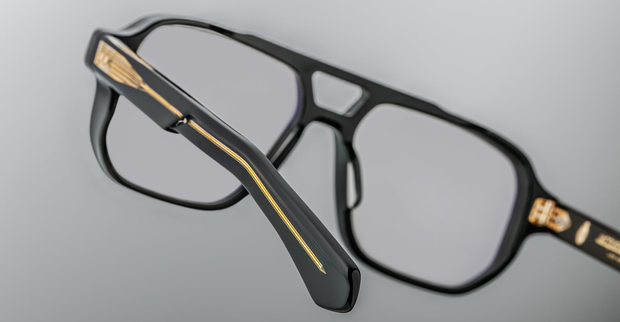 Close-up of the Jacques Marie Mage Evans optical glasses, featuring black oversized acetate frames with gold detailing on the arms and hinges, set against a neutral background.