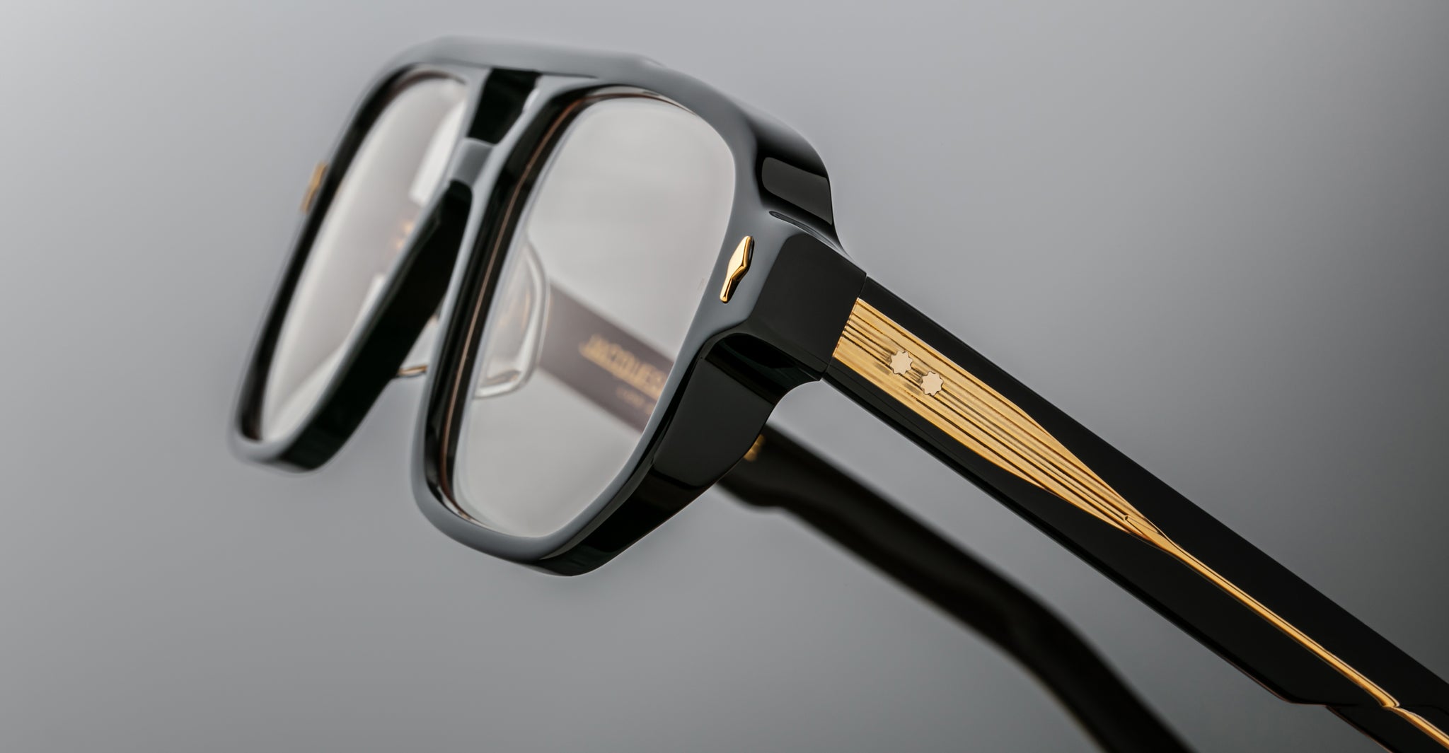 Close-up of Jacques Marie Mage Evans black oversized acetate eyeglasses featuring gold detailing and small star accents on the temples, set against a gray background.