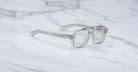 Jacques Marie Mage Evans clear-framed handcrafted optical glasses with transparent lenses are displayed on a white marble surface.