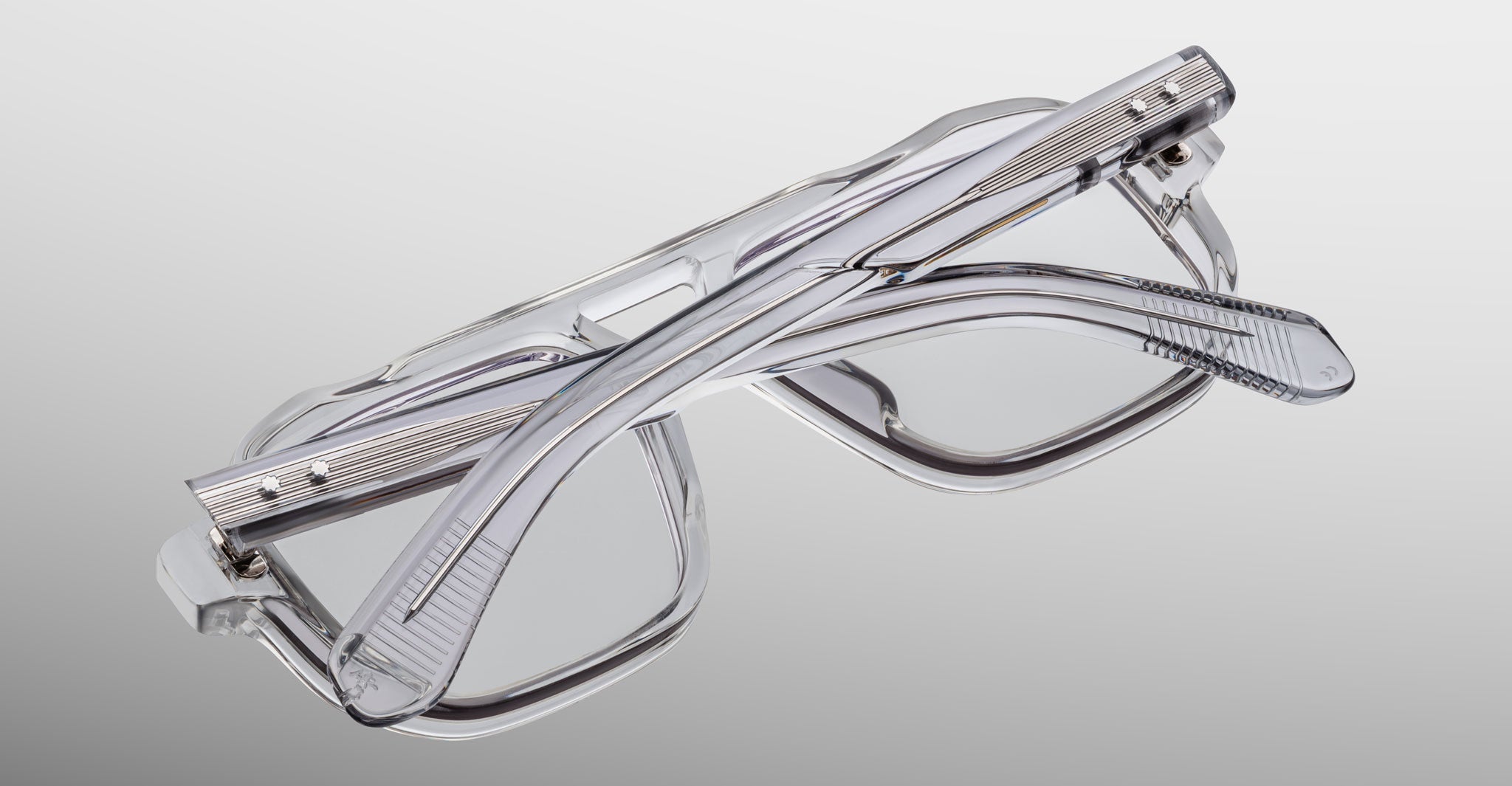 The Jacques Marie Mage Evans, a pair of handcrafted rectangular optical glasses by Jacques Marie Mage, is folded and set on a light gray gradient background.