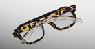 A pair of Jacques Marie Mage Evans tortoiseshell glasses stacked with clear handcrafted optical rectangular frames, both by Jacques Marie Mage, shown on a plain background.