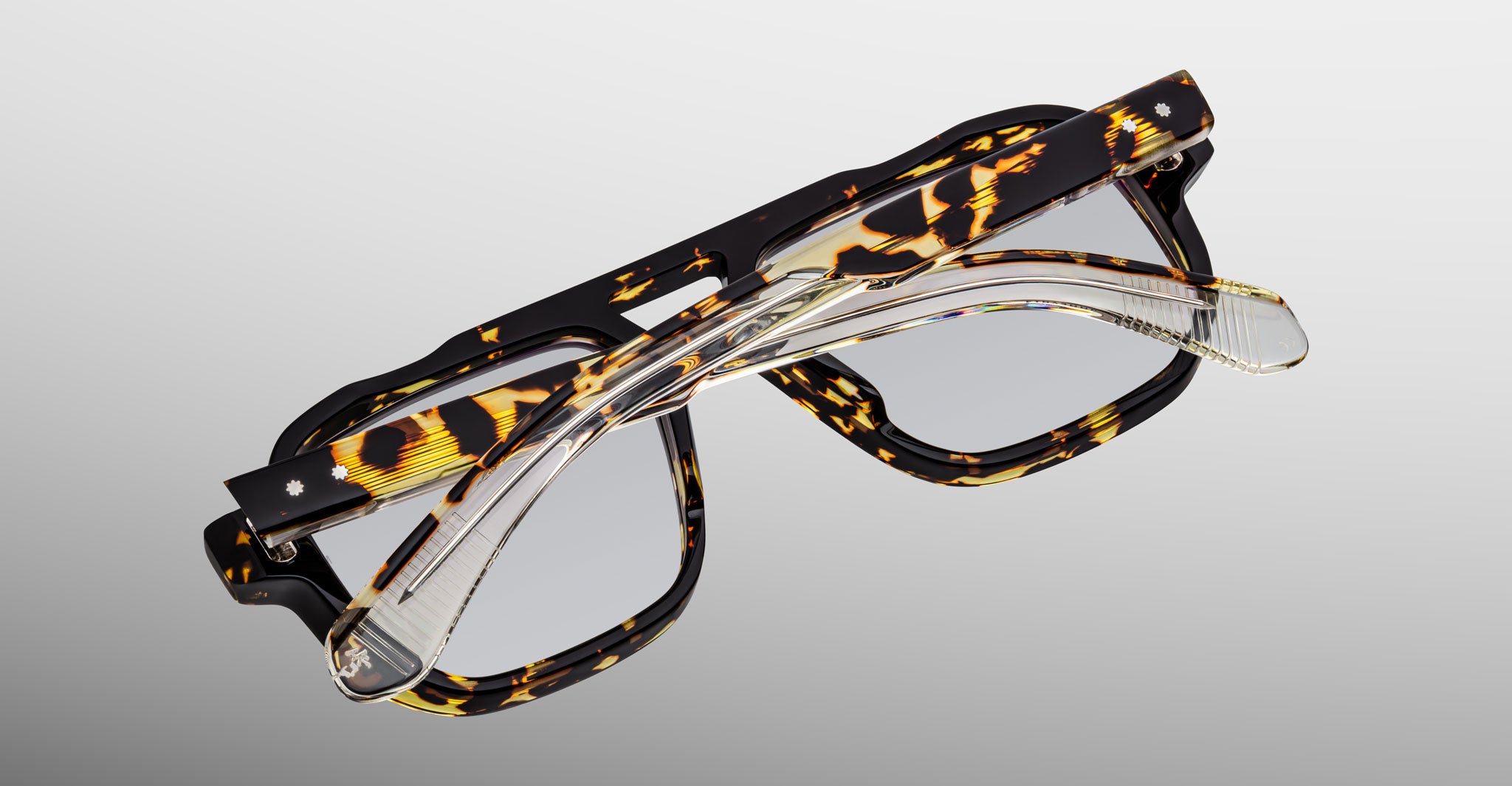 A pair of Jacques Marie Mage Evans tortoiseshell glasses stacked with clear handcrafted optical rectangular frames, both by Jacques Marie Mage, shown on a plain background.