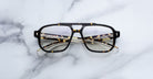 The Jacques Marie Mage Evans eyeglasses, featuring an oversized tortoiseshell acetate frame and clear lenses, rest on a white marble surface.