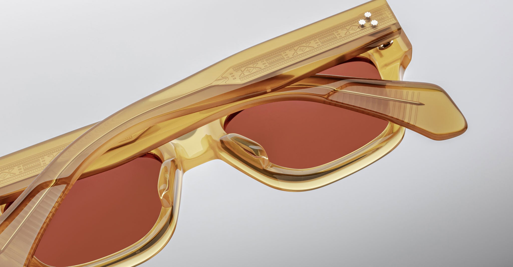Close-up of Jacques Marie Mage Fellini sunglasses with amber frame, brown polarized lenses, and etched detailing on the frames.
