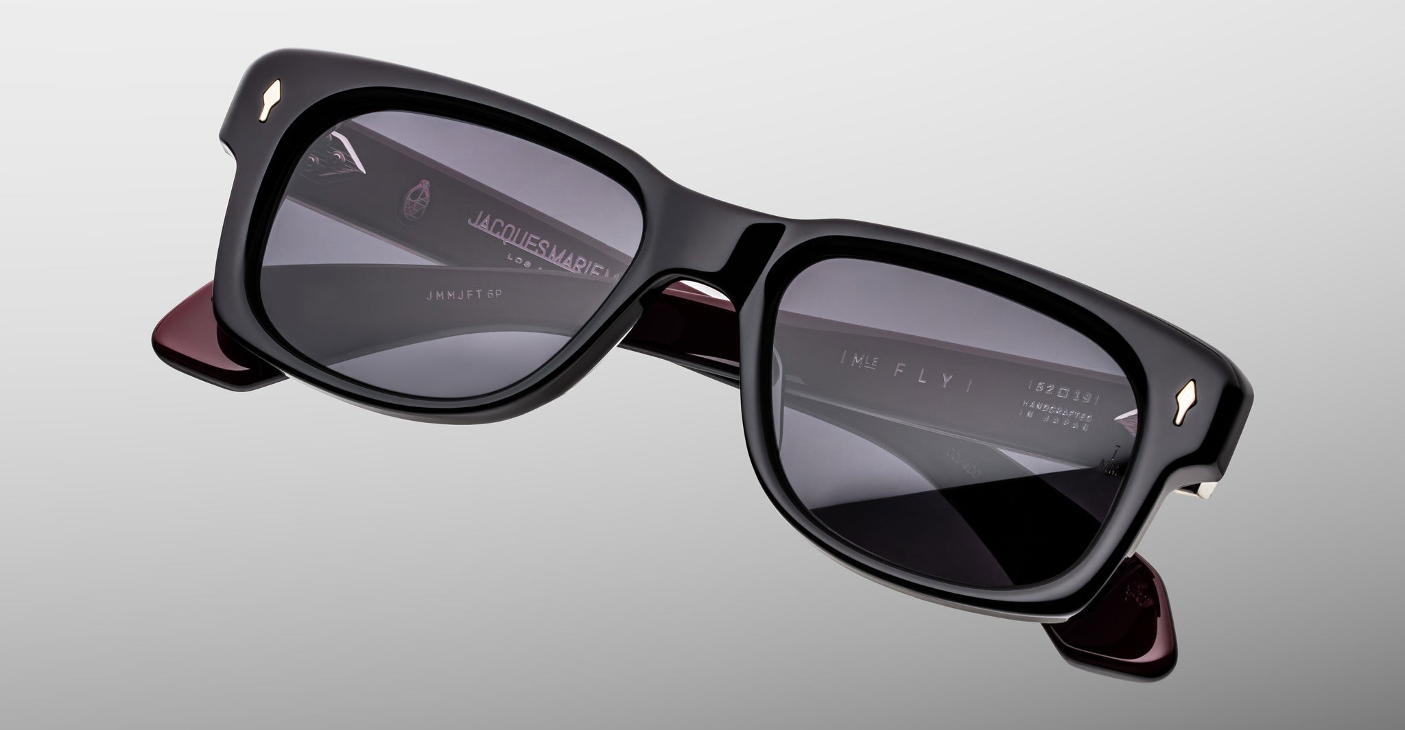 Jacques Marie Mage Fly eyeglasses, rectangular black frames with dark lenses, gold corners, and visible inner arm branding.