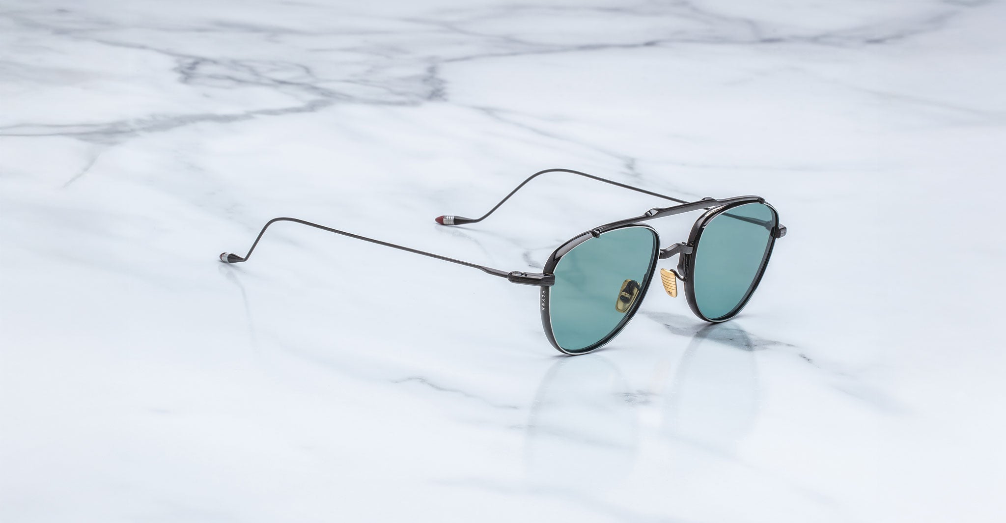Jacques Marie Mage Flynn sunglasses feature round green lenses and thin black frames, shown from above.