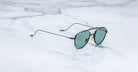 Jacques Marie Mage Flynn sunglasses feature round green lenses and thin black frames, shown from above.