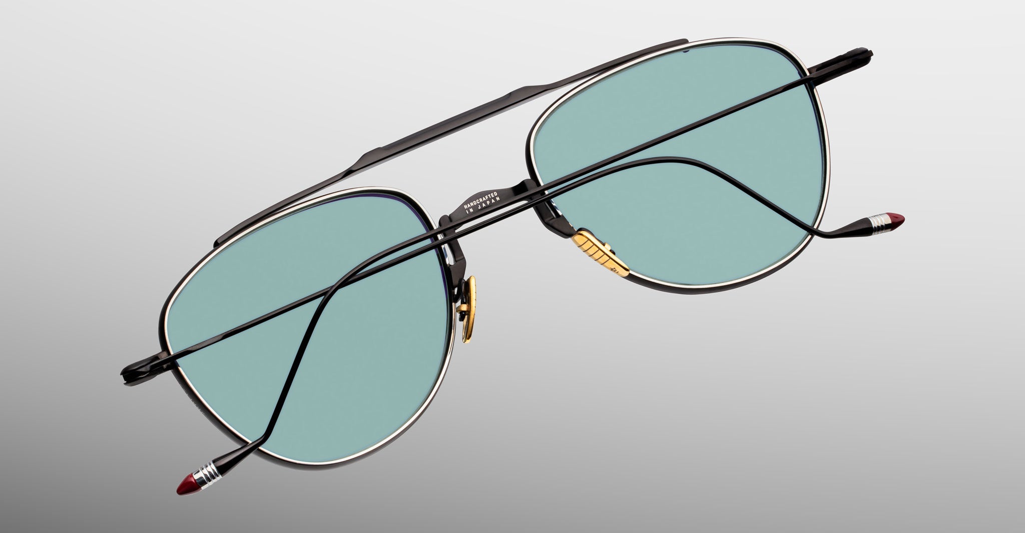 Jacques Marie Mage Flynn aviator sunglasses with green lenses and red-tipped temples, flat lay view.