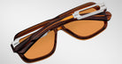Jacques Marie Mage Fugue sunglasses with orange lenses and silver hinges, shown folded from a top-down angle.