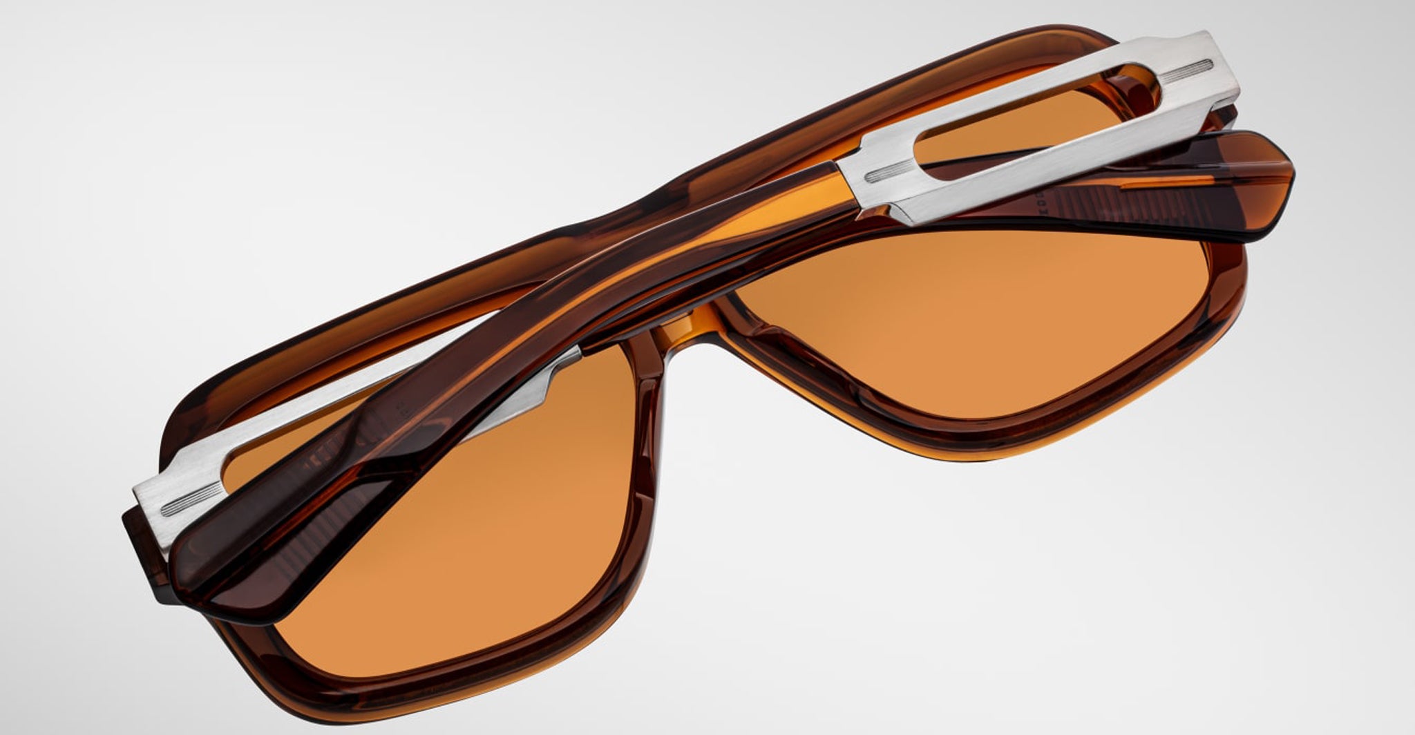 Jacques Marie Mage Fugue sunglasses with orange lenses and silver hinges, shown folded from a top-down angle.