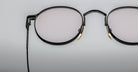 Close-up of Jacques Marie Mage Full Metal Jacket eyeglasses—black round frames with gold accents—set against a plain light gray background.