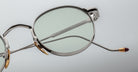 Close-up of Jacques Marie Mage Full Metal Jacket round silver metal eyeglasses featuring thin frames, gold nose pads, and a red-tipped temple arm against a light gray background.