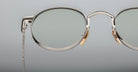 Close-up of Jacques Marie Mage Full Metal Jacket eyeglasses featuring silver oval thin metal frames, clear lenses, and gold nose pads set against a plain, light gray background.