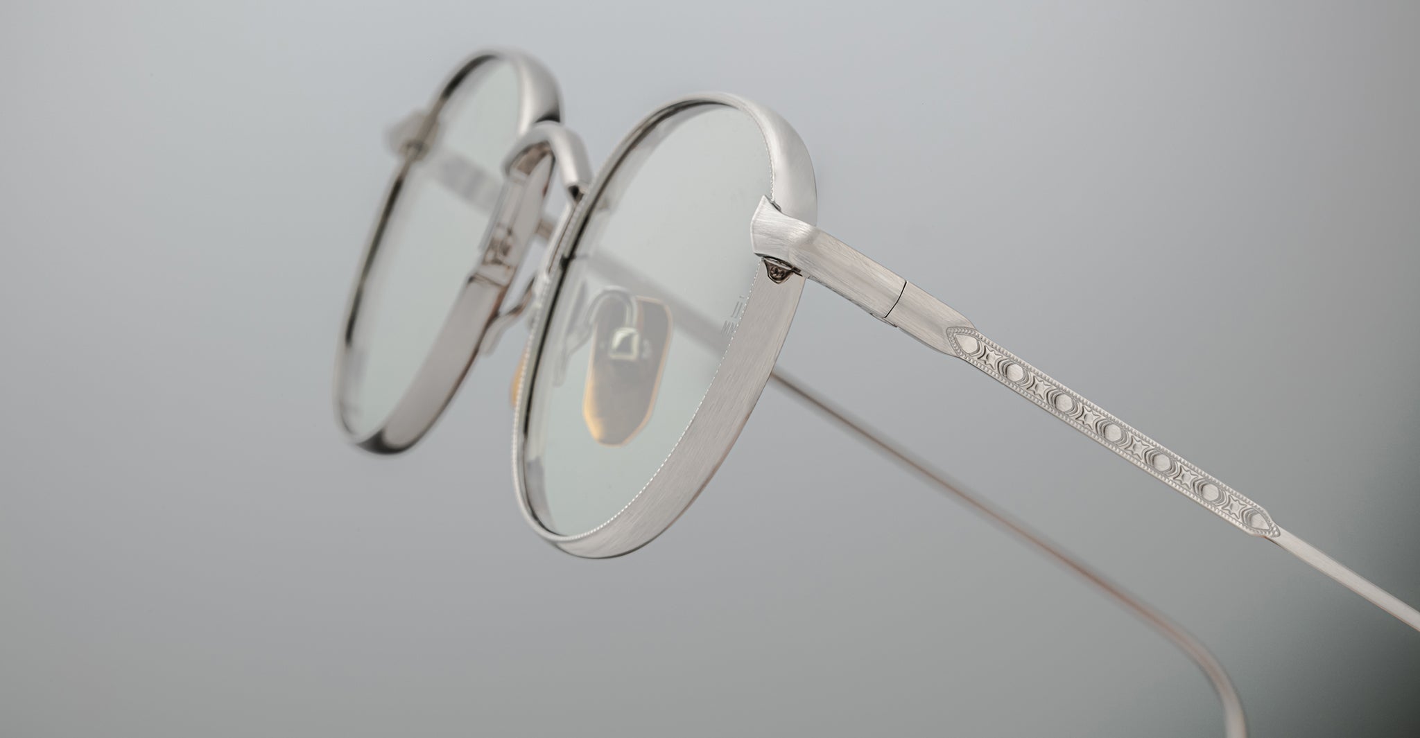 Close-up of Jacques Marie Mage Full Metal Jacket round, silver-framed eyeglasses with clear lenses against a plain light grey background, highlighting the intricate metalwork along the temple arm.