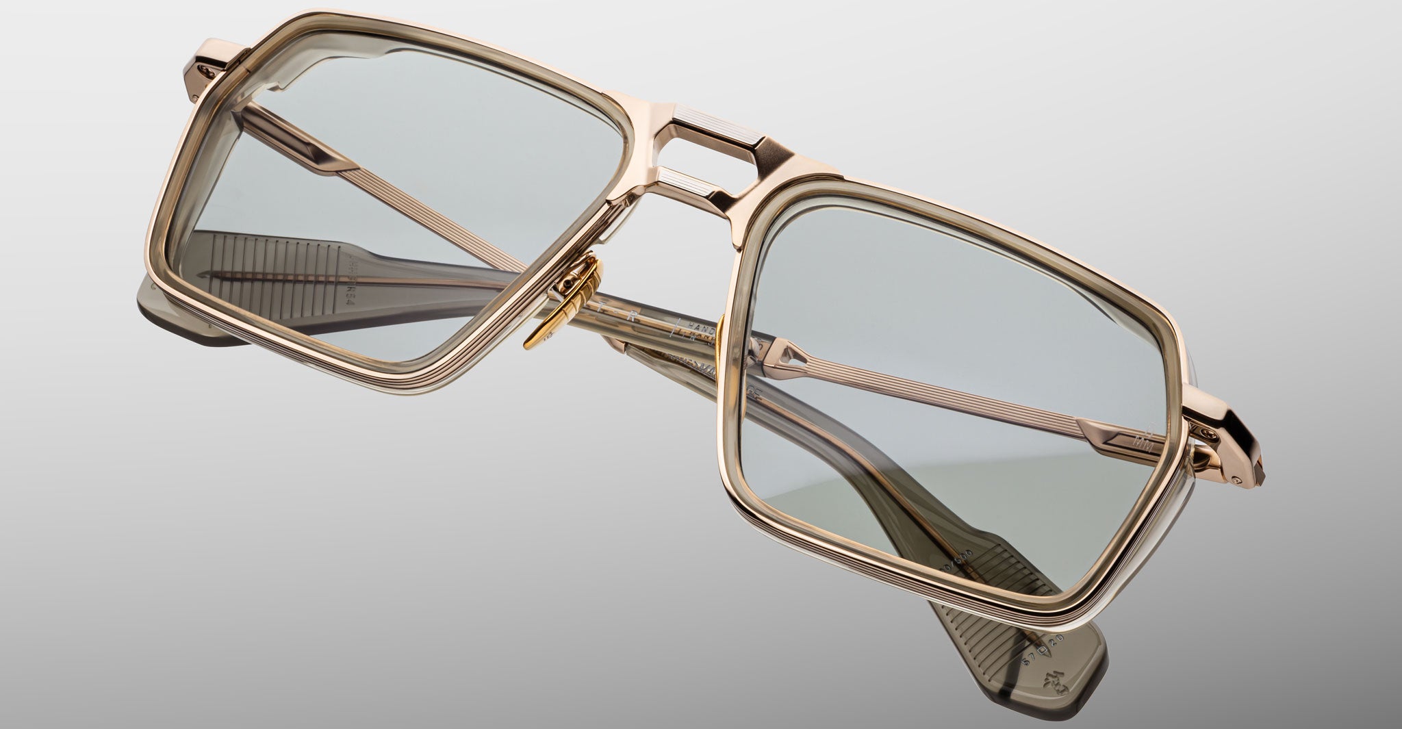 The Jacques Marie Mage GT-R features rectangular gold metal frames and light gray tinted lenses, shown angled against a matching light gray background.