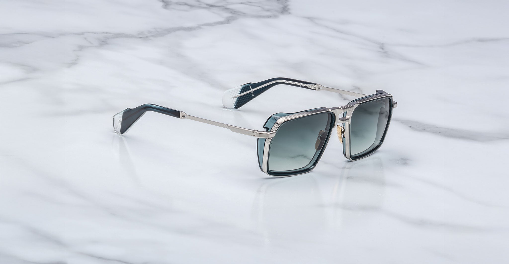 Jacques Marie Mage GT-R rectangular sunglasses with silver metal frames and dark tinted lenses rest on a white marble surface.