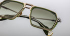 Close-up of Jacques Marie Mage GT-R rectangular sunglasses featuring gold metal frames, green accents, and green-tinted lenses, set against a plain light background.