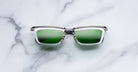 Jacques Marie Mage Gaspard clear-framed mirrored sunglasses with green lenses, top-down view.