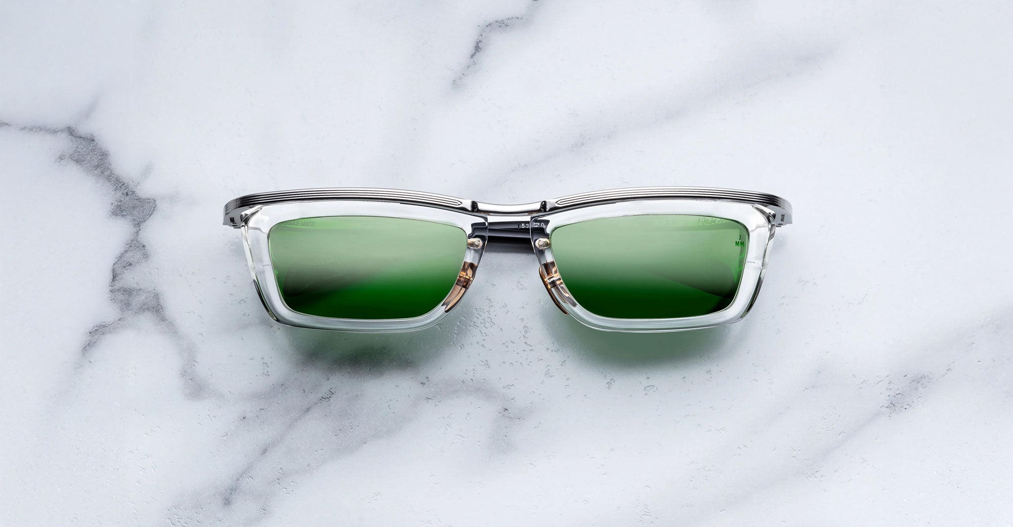 Jacques Marie Mage Gaspard clear-framed mirrored sunglasses with green lenses, top-down view.