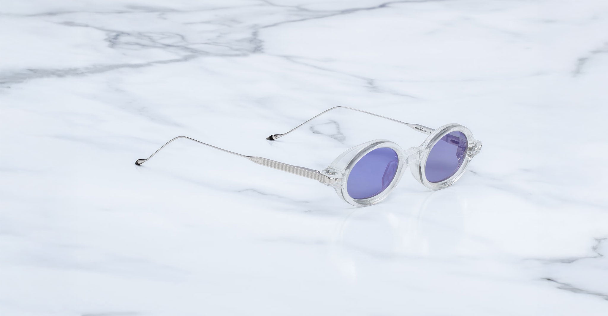 Jacques Marie Mage Balthazar sunglasses with clear round frames and purple lenses, viewed from above.