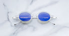 Jacques Marie Mage Balthazar round clear sunglasses with blue lenses, top view, eyewear displayed on surface.