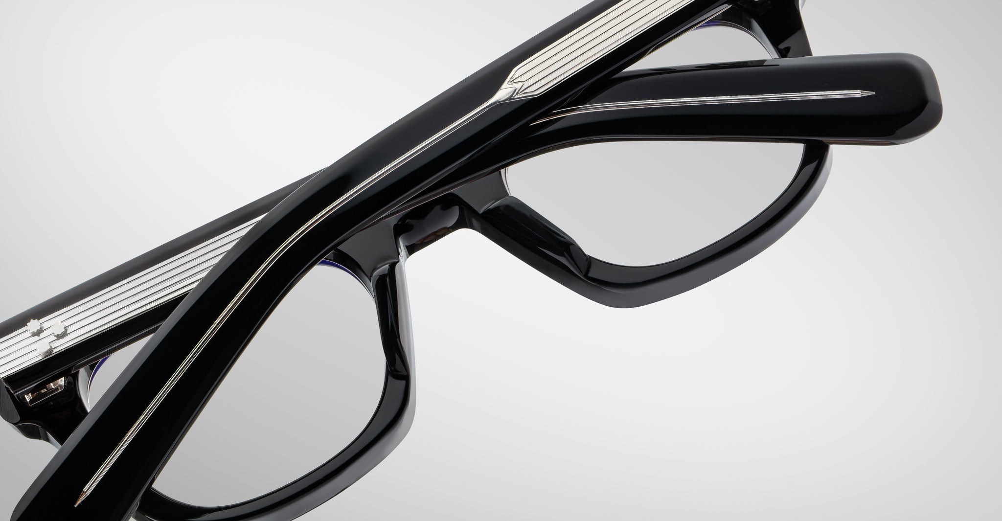 Close-up of Jacques Marie Mage Godard black eyeglasses with silver-detailed temples, folded against a plain light gray background.