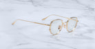 Jacques Marie Mage Hartana eyeglasses with a gold metal frame and clear lenses are displayed on a white marble surface.