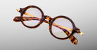 Jacques Marie Mage Hartigan in Argyle, round tortoiseshell acetate eyeglasses shown from a close angled front view, featuring a keyhole bridge, exposed metal core temples, and subtle purple anti-reflective lens coating.