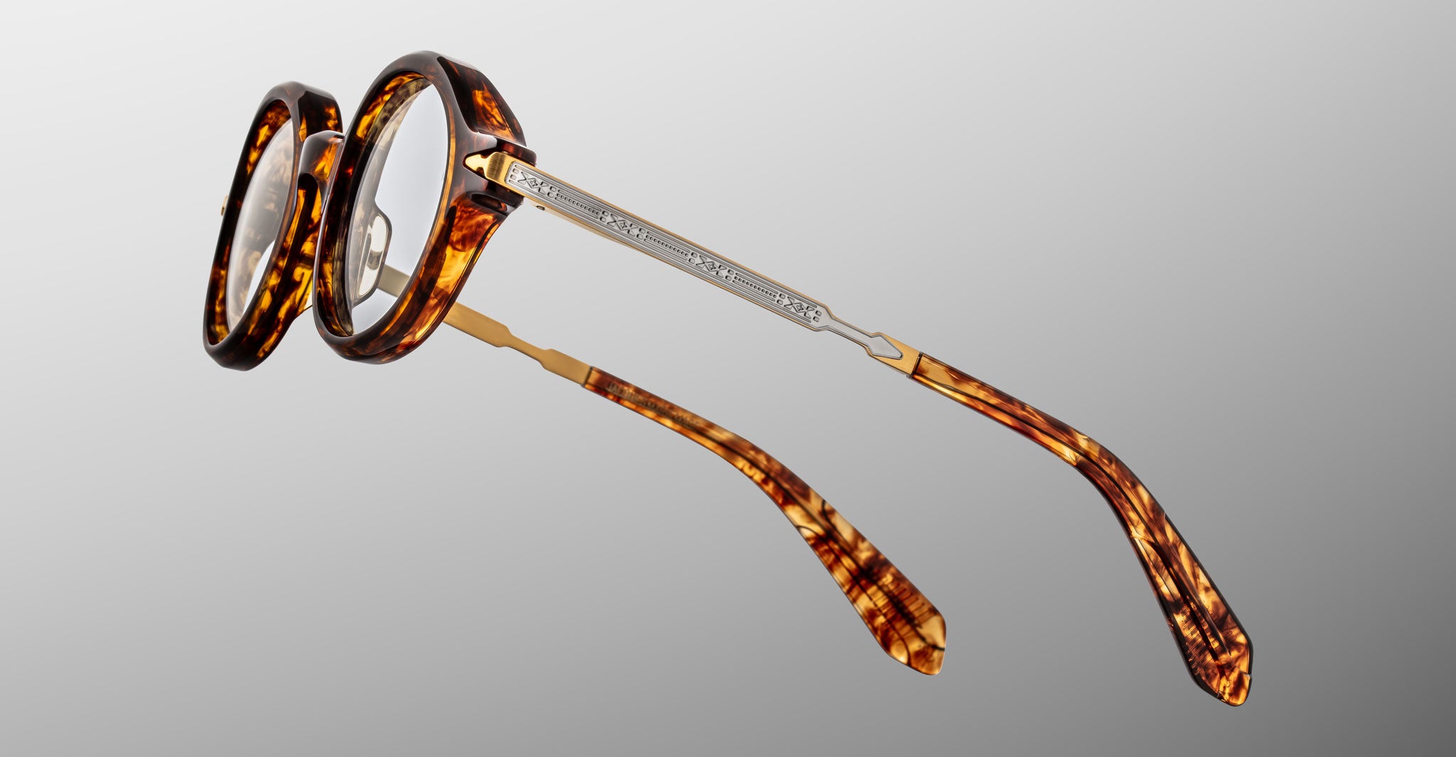Jacques Marie Mage Hartigan in Argyle, round tortoiseshell acetate eyeglasses shown from a rear side angle, highlighting engraved metal core temples, custom hinge details, and sculpted temple tips with clear demo lenses.
