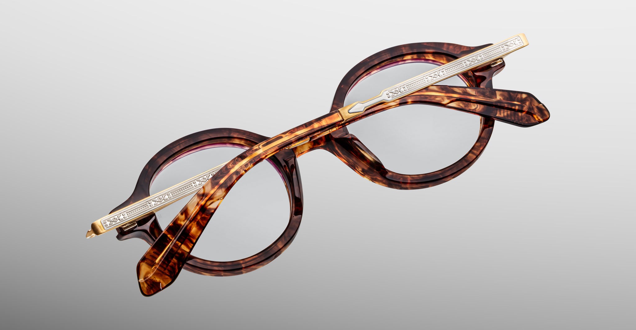 Jacques Marie Mage Hartigan in Argyle, round tortoiseshell acetate eyeglasses shown from an angled top view, highlighting engraved metal core temples, keyhole bridge, and sculpted temple tips with clear demo lenses.
