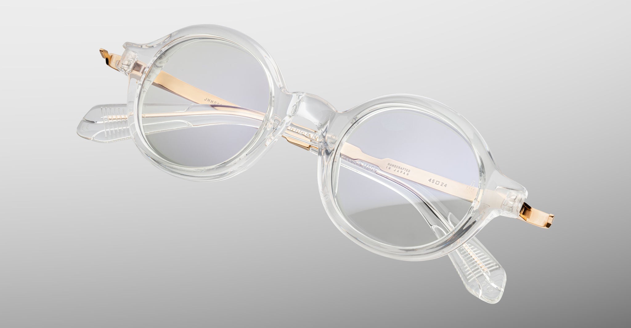 Jacques Marie Mage Hartigan in Clear, round transparent acetate eyeglasses shown from a close angled front view, featuring a keyhole bridge, exposed metal core temples, and subtle anti-reflective lens coating.