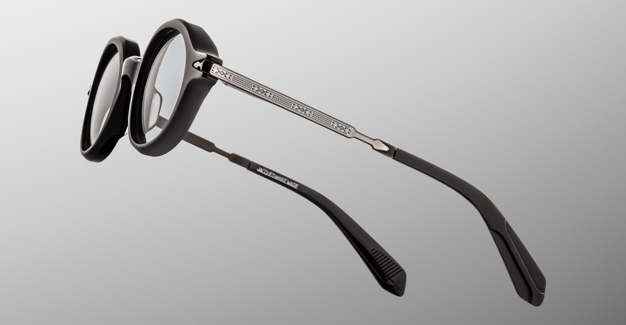 Jacques Marie Mage Hartigan in Phantom, round black acetate eyeglasses shown from a rear side angle, highlighting engraved metal core temples, custom hinge details, and sculpted temple tips with clear demo lenses.