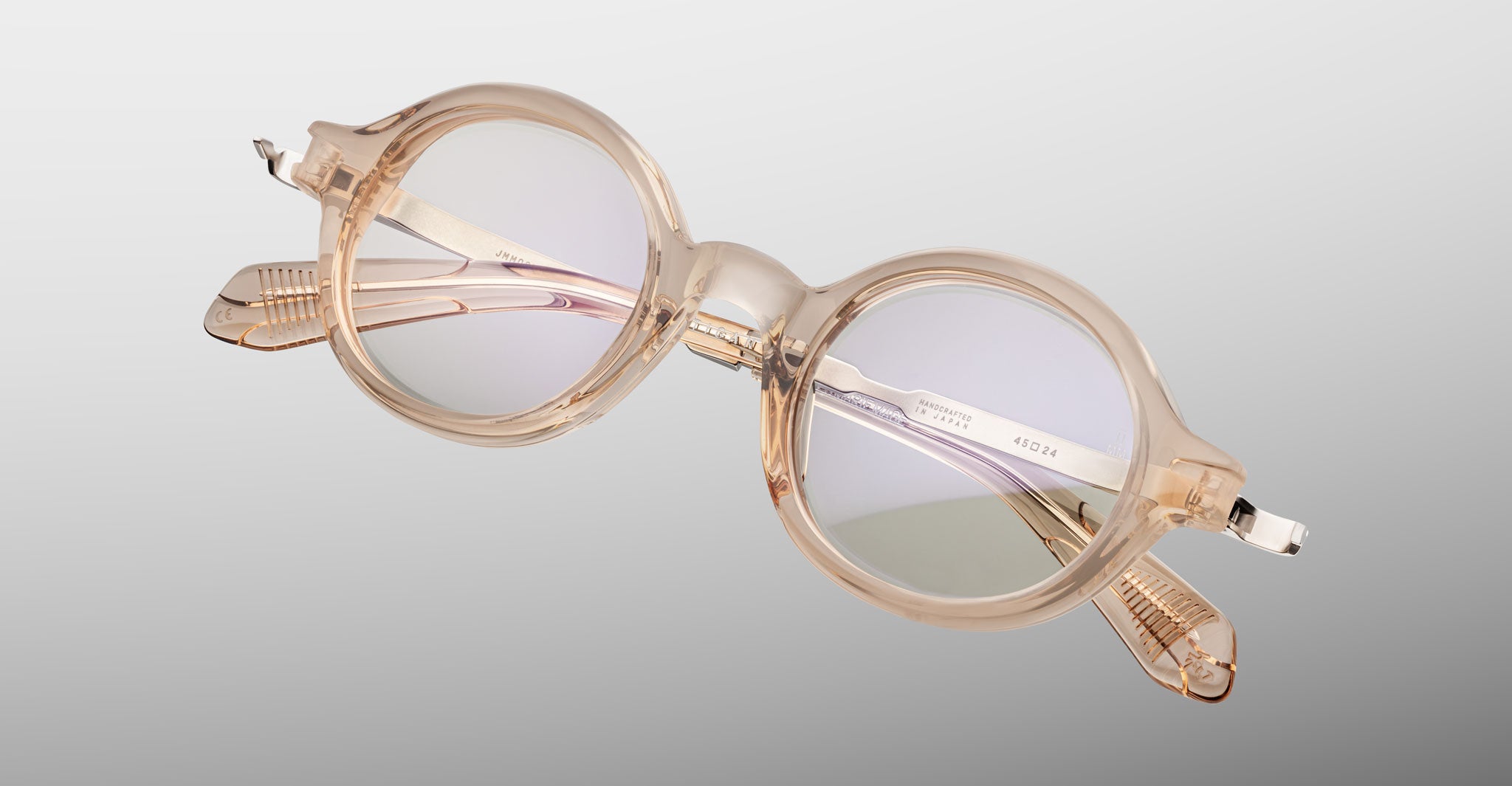 Jacques Marie Mage Hartigan in Sand, round translucent beige acetate eyeglasses shown from a close angled front view, featuring a keyhole bridge, exposed metal core temples, and sculpted temple tips with subtle anti-reflective lens coating.
