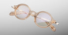 Jacques Marie Mage Hartigan in Sand, round translucent beige acetate eyeglasses shown from a close angled front view, featuring a keyhole bridge, exposed metal core temples, and sculpted temple tips with subtle anti-reflective lens coating.
