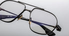 Close-up of Jacques Marie Mage Hollywood eyeglasses featuring stylish black rims, gold nose pads, and clear lenses on a light gray surface. One temple arm reads HANDCRAFTED IN JAPAN.