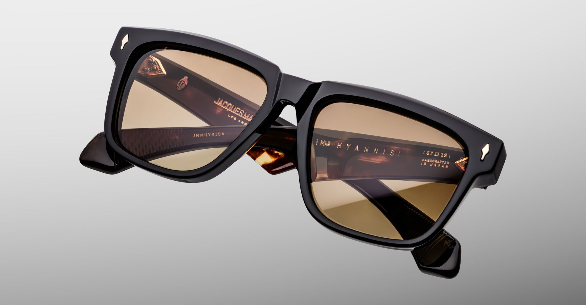 Jacques Marie Mage Hyannis in Noir 15 black square sunglasses, close-up view, brown-tinted lenses, gold branding on inner arms visible.