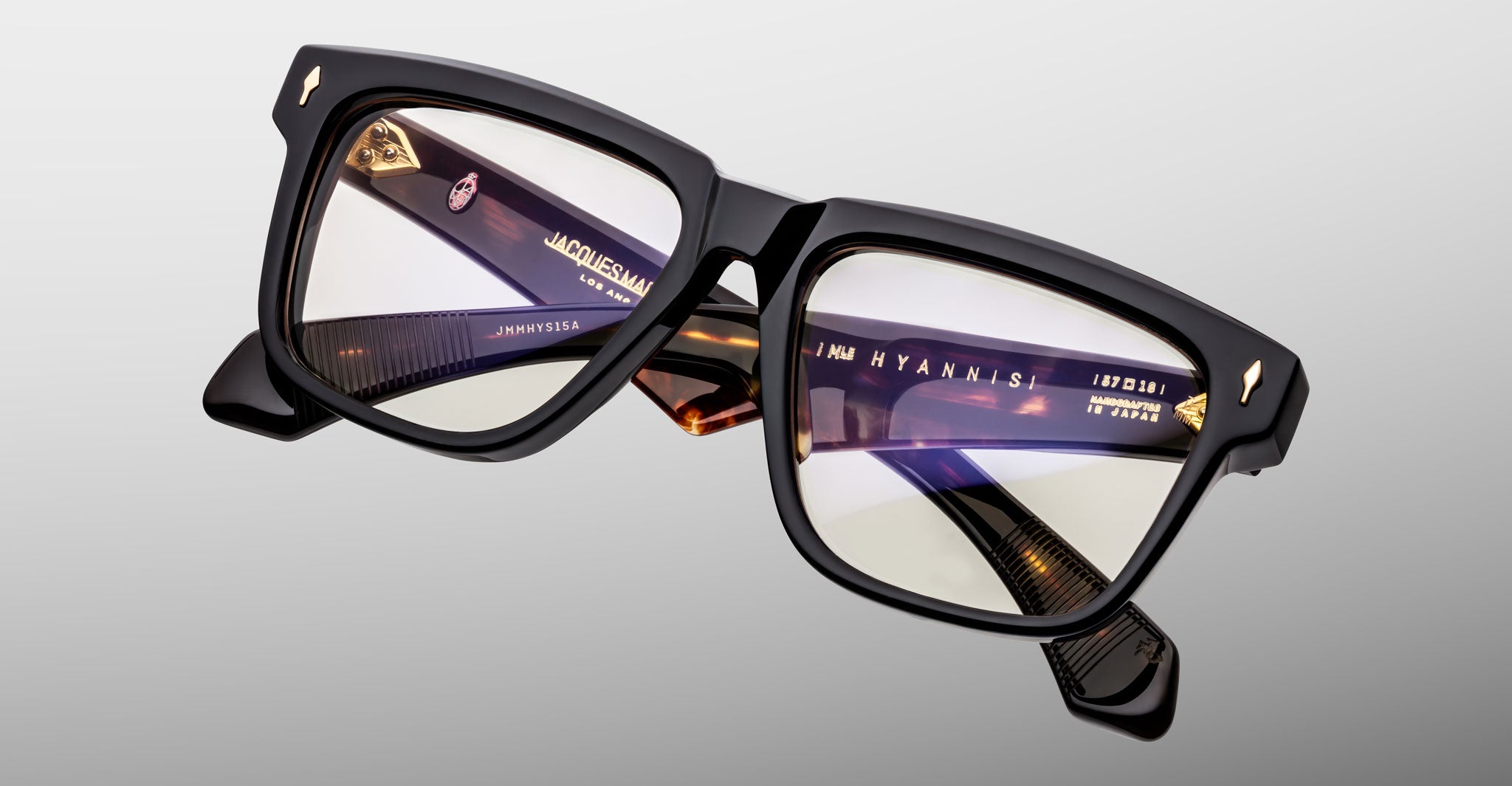 Close-up of Jacques Marie Mage Hyannis in Noir 15 eyeglasses, black thick-rimmed frames with clear lenses and gold accents, front view.