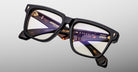 Close-up of Jacques Marie Mage Hyannis in Noir 15 eyeglasses, black thick-rimmed frames with clear lenses and gold accents, front view.