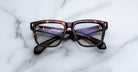 Jacques Marie Mage Hyannis tortoiseshell rectangular eyeglass frames with thick edges displayed elegantly on a white marble surface.
