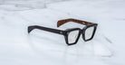 Jacques Marie Mage Ichikawa black rectangular eyeglasses with thick frames and brown inner arms, front angle view.