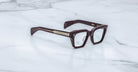 Jacques Marie Mage Ichikawa brown rectangular eyeglasses with thick frames and gold accents, shown from the front.