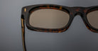 Close-up of the right side of Jacques Marie Mage Initials rectangular tortoiseshell micro-frame sunglasses with brown-tinted lenses, set against a gray background.