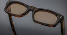 Close-up of Jacques Marie Mage Initials rectangular eyeglasses in brown tortoiseshell with tinted lenses, highlighting the brand’s limited-edition frames against a plain background.